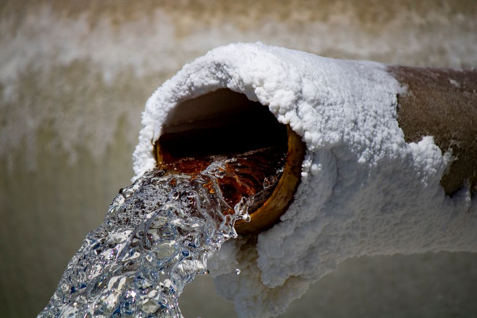 Rusty pipe with heavy white mineral scale deposits and flowing water, illustrating hard water pipe damage in Riverside County homes
