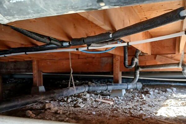 Crawl space with new water lines hung from the floor framing