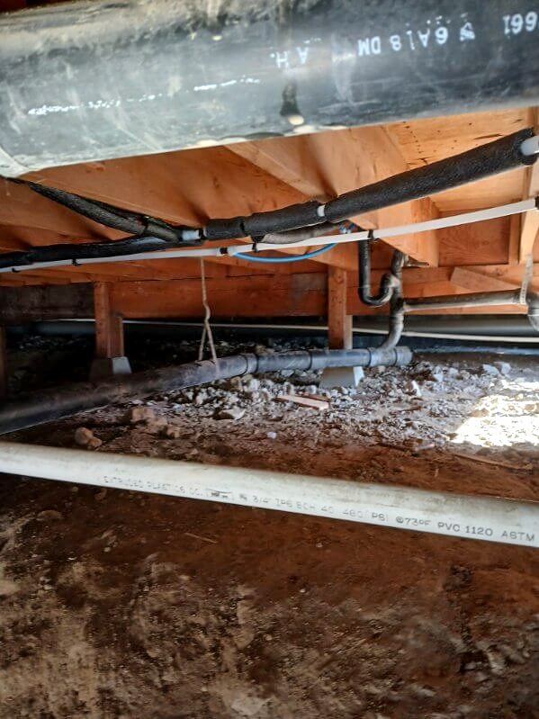Crawl space with new water lines hung from the floor framing